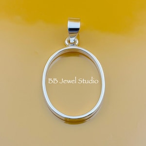 Könnte beinhalten: Ein silberfarbener ovaler Anhänger mit einer Schlaufe oben. Der Anhänger hat eine klare Mitte und der Text "BB Jewel Studio" ist auf der Vorderseite aufgedruckt. Der Hintergrund ist einfarbig gelb.