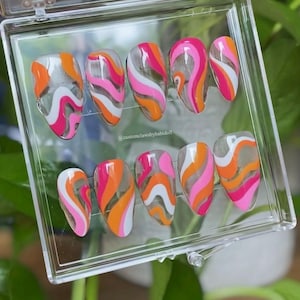 May include: A set of press-on nails in a clear plastic case. Each nail features a retro design with wavy stripes in pink, orange, and white. The nails are almond-shaped and appear glossy. The text "@customclawsbybabidoll" is visible.