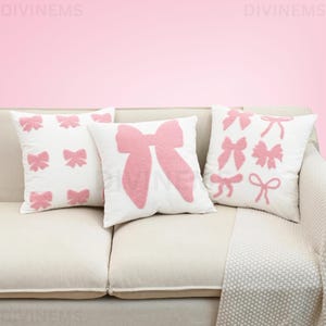 Peut inclure: Trois coussins blancs avec des motifs de nœuds roses reposent sur un canapé beige. Les nœuds varient en style et en taille, certains coussins présentant plusieurs petits nœuds et d'autres un seul grand nœud. Les coussins ajoutent une touche de fantaisie à la pièce.