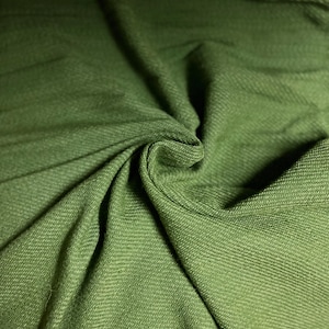 May include: Close-up of olive green fabric with a textured weave. The fabric is draped and folded, creating shadows and highlights that emphasize its texture and color. The material appears soft and pliable.