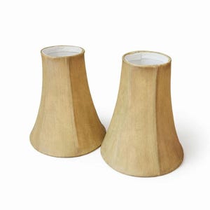 Puede incluir: Dos pantallas de lámpara beige con un diseño geométrico acampanado. Las pantallas tienen un color beige claro y un interior blanco. Las pantallas están diseñadas para colocarse sobre una base de lámpara y difunden la luz.