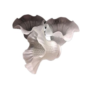 May include: Three-piece decorative glass sculpture with a floral design. The sculpture features three flower-like forms in shades of white and gray. The petals have a ruffled edge and textured surface.