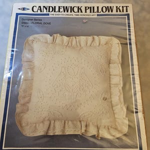Puede incluir: Kit de almohada Candlewick con un diseño floral de paloma. La almohada mide 35,5 x 35,5 cm y presenta una tela color crema con detalles bordados y un borde con volantes. El kit está empaquetado en una caja con el texto "Candlewick Pillow Kit".