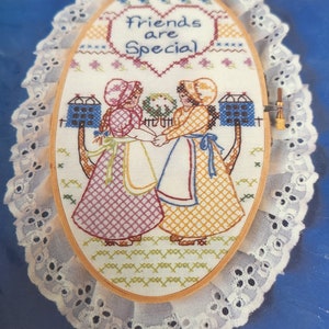 May include: A cross stitch kit with a 5 inch by 9 inch wooden hoop, stamped fabric, embroidery floss, needle, and lace. The design features two girls holding hands with the text "Friends are Special".