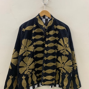 May include: Black jacket with gold floral and abstract embroidery. The jacket has a high collar and a zipper closure. The lining is black and white checkered. The jacket is hanging on a wooden hanger.