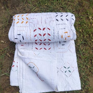 Puede incluir: Textil blanco con patrones bordados coloridos. El textil está doblado y colocado sobre hierba. El bordado incluye diseños rojos, naranjas, negros y verdes. El texto "Shot on OnePlus SellerTextileExport" es visible en la esquina inferior izquierda.