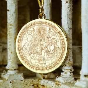 May include: A gold-colored pendant necklace featuring a detailed engraved design of a figure riding an animal. The pendant is circular and hangs from a delicate chain. The background is a weathered, architectural structure.