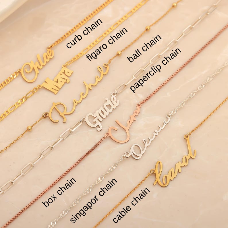 May include: A collection of gold and silver name necklaces with various chain styles, including curb, figaro, ball, paperclip, box, singapor, and cable chains. Each necklace features a different name in a cursive font.