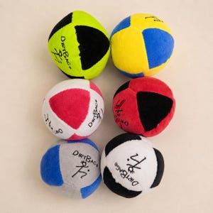 Puede incluir: Seis pelotas Dirtbag multicolores. Las pelotas están en varias combinaciones de colores: verde y negro, amarillo y azul, rojo y negro, blanco y rojo, azul y gris, y negro y blanco. Cada pelota tiene el logo de Dirtbag y una figura estilizada.