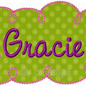 Puede incluir: Una aplicación en forma de nube verde y rosa con lunares blancos y el nombre "Gracie" bordado en morado. El texto "silly cat designs" también es visible en la parte inferior de la aplicación.