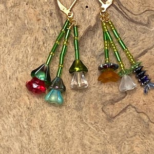 May include: A pair of dangle earrings with gold-colored lever-back closures. Each earring features a cluster of colorful glass beads and flower-shaped charms in red, green, blue, orange, and clear. The beads are strung on green wire.