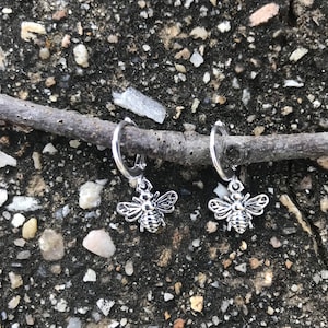 May include: A pair of silver hoop earrings with a silver bee charm hanging from each hoop.