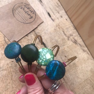 May include: Four gold wire bracelets with different colored round ceramic beads. The beads are green, blue, and white with green speckles.