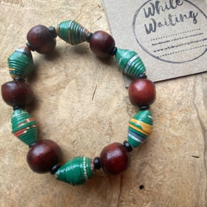 May include: A green and brown paper bead bracelet with a wooden tag that says "While Waiting".