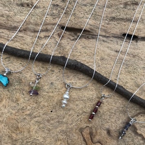 May include: Six silver necklaces with different gemstone pendants. The pendants include a turquoise stone, a cluster of multi-colored stones, a pearl, a row of red stones, and two rows of blue stones.