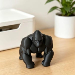 May include: A matte black figurine of a gorilla in a quadrupedal stance, featuring a muscular build with defined chest, shoulder, and arm muscles. The sculpture has a smooth, solid surface and is depicted in a forward-facing, alert posture.