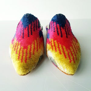 May include: A pair of pointed-toe mules with a colorful ikat pattern in shades of pink, yellow, blue, and white.