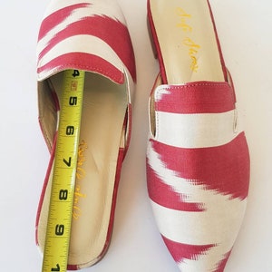 May include: A pair of red and white striped pointed toe mules with a fabric upper and a leather insole. The mules are 8 inches long.