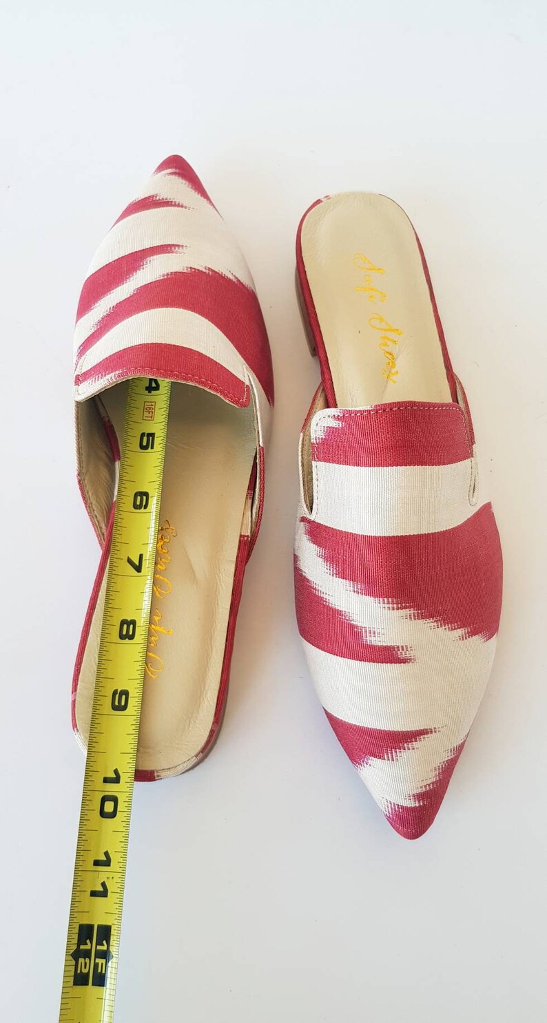 May include: A pair of red and white striped pointed toe mules with a fabric upper and a leather insole. The mules are 8 inches long.