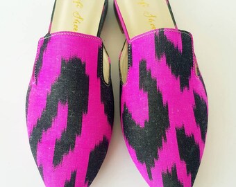 May include: A pair of pink and black patterned mules with a pointed toe. The mules have a gold inscription on the inside that reads "Aft Studio".