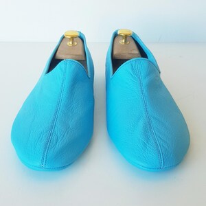 Puede incluir: Un par de zapatillas de cuero azul claro. Las zapatillas tienen una punta puntiaguda y un diseño sencillo.