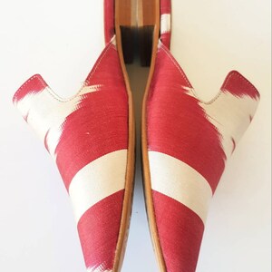 May include: A pair of red and white patterned fabric mules with wooden heels.