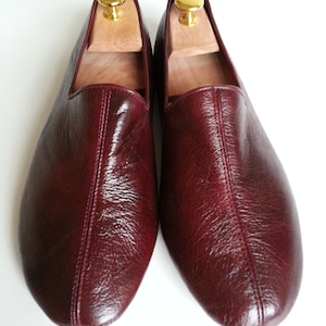 May include: A pair of burgundy leather slippers with a pointed toe and a simple design. The slippers are made of soft, supple leather and have a comfortable fit.