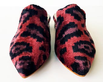 May include: A pair of slip-on shoes with a red and black leopard print pattern. The shoes have a pointed toe and a low heel. The shoes are made of a soft, velvety material.