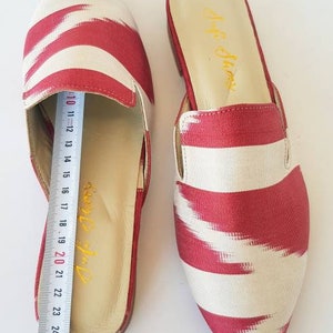 May include: A pair of red and white striped pointed-toe slip-on shoes. The shoes have a cream-colored insole and a red and white striped fabric upper. The shoes are 25 cm long.