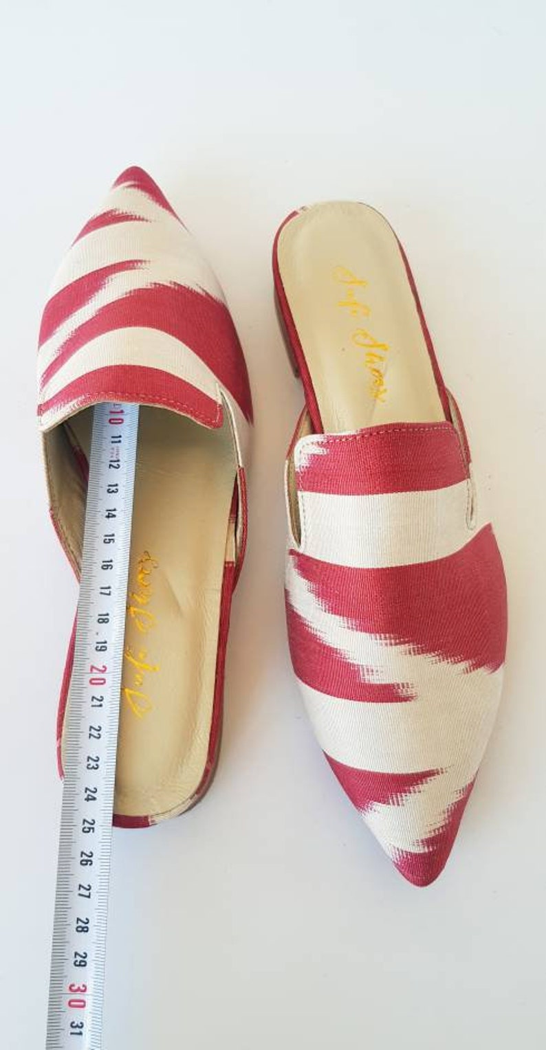 May include: A pair of red and white striped pointed-toe slip-on shoes. The shoes have a cream-colored insole and a red and white striped fabric upper. The shoes are 25 cm long.