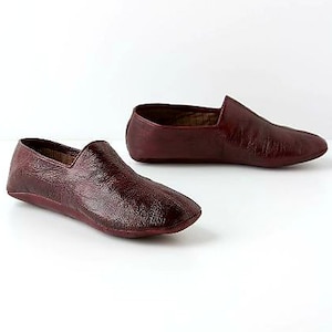 May include: Two pairs of burgundy leather slippers with a textured finish. The slippers have a pointed toe and a flat sole.