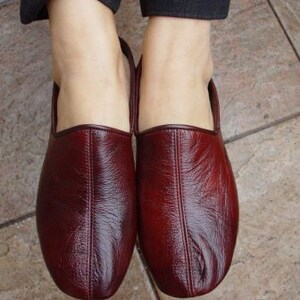 May include: A pair of burgundy leather slippers with a pointed toe and a closed back.