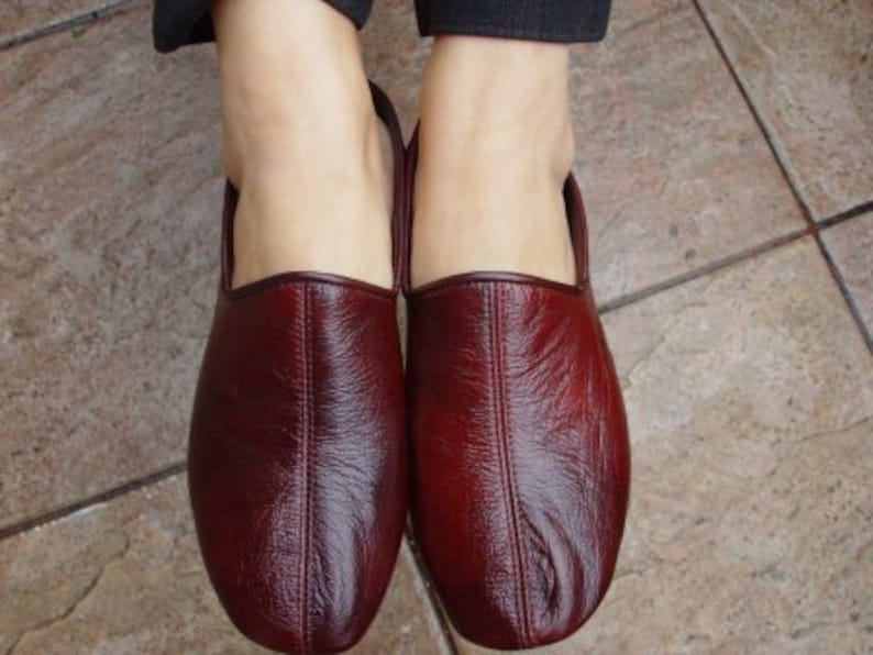 May include: A pair of burgundy leather slippers with a pointed toe and a closed back.