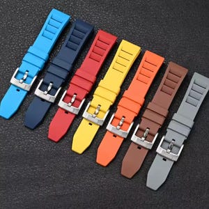 May include: A selection of vibrant watch straps in shades of blue, navy, red, yellow, orange, brown, and grey. Each strap has a silver buckle and a textured design. The straps are made of a flexible material.