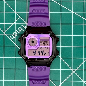 May include: A digital wristwatch with a purple strap and a black case. The watch face features a purple background, a circular analog-style display, a world map graphic, and a digital time display showing 4:44:21 with the text LON T-3.