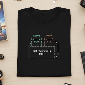 May include: Black t-shirt with a graphic design featuring the text "Alive" and "Dead" above a box labelled "Schrödinger's Box." The design uses ASCII art to depict a cat in the box. A fun, science-themed tee.
