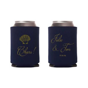 May include: Two navy blue can coolers with gold lettering. One cooler has a seashell design and the text "Cheers!" The other cooler has the text "Julie & Tom 6.19.24".