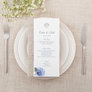 May include: A wedding menu card with a blue seashell design and blue floral accents. The menu lists the courses: First Course, Second Course, and Dessert. The text reads: "Caline & Scott, May 20, 2022".