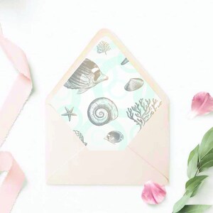 May include: A pink envelope with a sea-themed liner. The liner features a pattern of seashells, starfish, coral, and fish in shades of gray and blue on a light blue background.