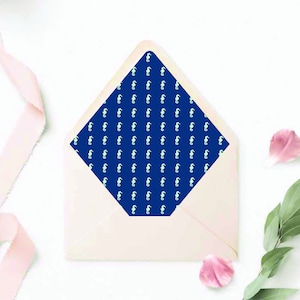 May include: A white envelope with a blue liner featuring a repeating pattern of white seahorses. The envelope is lying flat on a white surface with pink ribbon and pink flower petals.