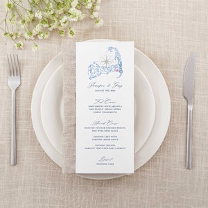 May include: A wedding menu card with a blue and white illustration of Cape Cod, Massachusetts. The menu includes a first course of baby greens with arugula and endive, a second course of roasted chicken breast with red wine demi glace, and a dessert of wedding cake.