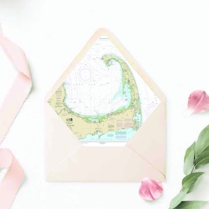 May include: A light pink envelope with a nautical map of Cape Cod inside. The envelope is on a white background with pink ribbon and flower petals.
