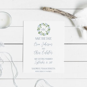 May include: Save the date card with a floral wreath design in blue and green. The wreath has the initials "E.C." in the center. The text reads "Save the Date, Erica Johnson and Chris Eubiston are getting married September 16, 2017, Sandwich, Massachusetts, www.theknot.com/frika".
