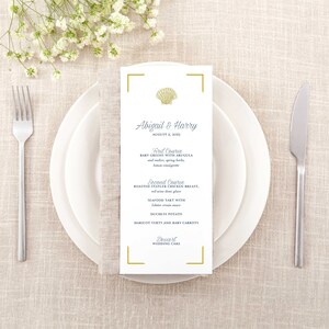 May include: A white wedding menu with a gold border and a seashell design. The menu lists the courses for the wedding reception: Baby Greens with Arugula, Roasted Statler Chicken Breast, Seafood Tart with Duchess Potato, Haricot Verts and Baby Carrots, and Wedding Cake.