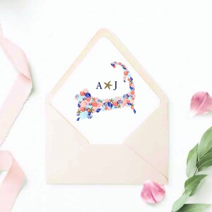 May include: A white envelope with a pink scalloped edge. The envelope contains a white card with a blue and pink seashell design in the shape of Cape Cod. The card also has the initials "A*J" in navy blue and gold.