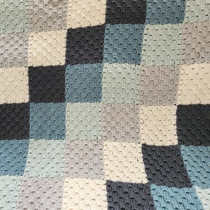 May include: A handmade crochet blanket with a patchwork design. The blanket features squares in shades of blue, gray, and cream. The textured surface and color palette create a cozy and inviting aesthetic. This blanket is perfect for home decor.