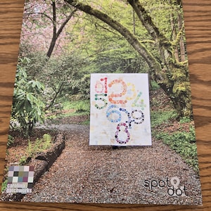 May include: A catalog featuring a scenic forest path with a small, colorful quilt design. The quilt design spells out "12 Sage" in a variety of colors. The catalog has the "carolina patchworks" and "spot dot" logos.