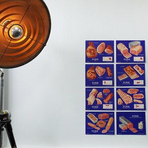 Puede incluir: Seis carteles azules que muestran diferentes cortes de cerdo, cada uno con la palabra "PORK". Los carteles están montados en una pared blanca, junto a una lámpara de pie industrial vintage con una gran pantalla circular.