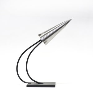 May include: A silver cone-shaped lamp with a black metal base and two curved arms. The lamp is on a white surface.