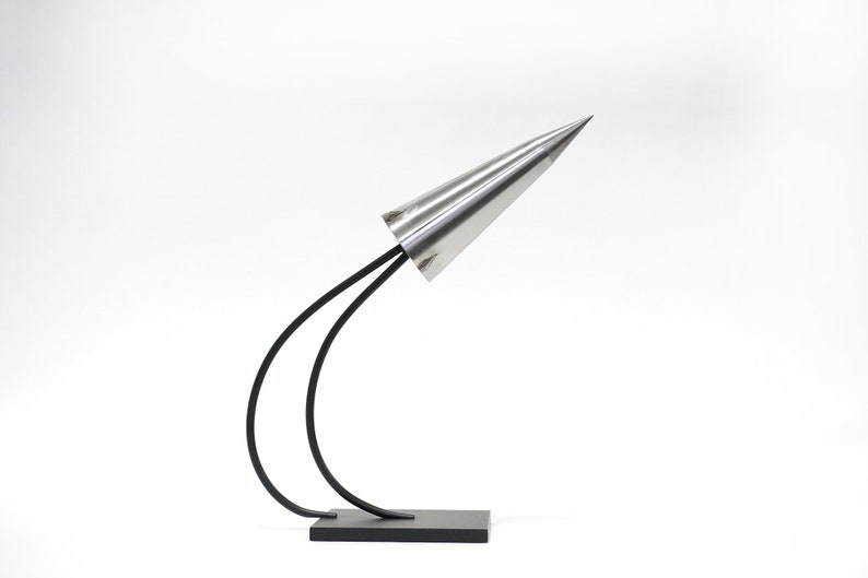 May include: A silver cone-shaped lamp with a black metal base and two curved arms. The lamp is on a white surface.